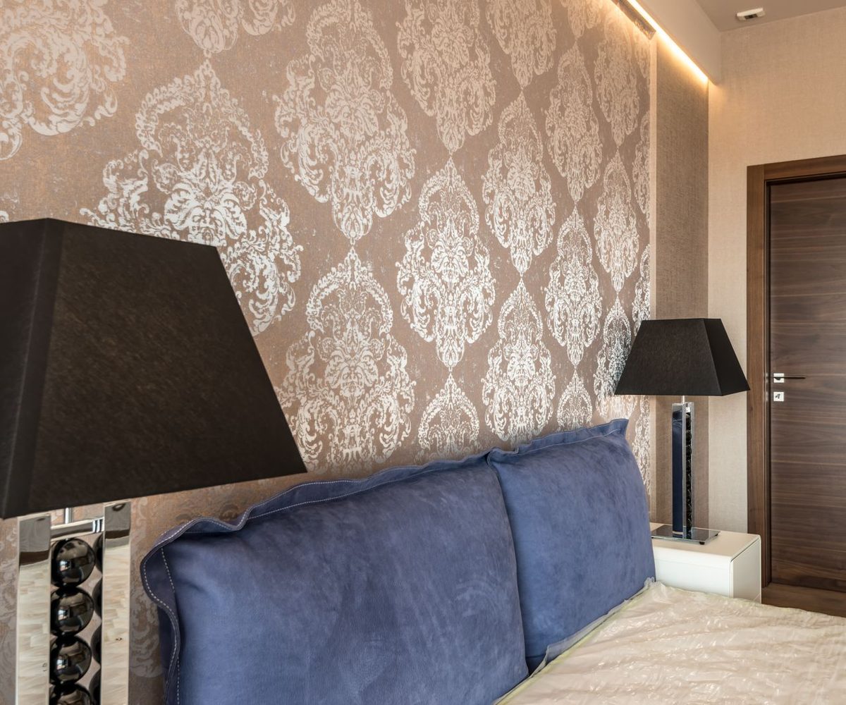 Close view of a copper damask wallpaper feature wall installed behind an upholstered headboard