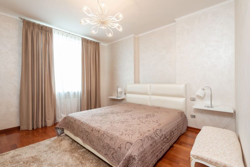 Soft neutral bedroom with subtle damask wall covering and a chandelier